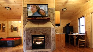 A cozy cabin interior with a stone fireplace, a television mounted above it, a pool table, and wooden walls.