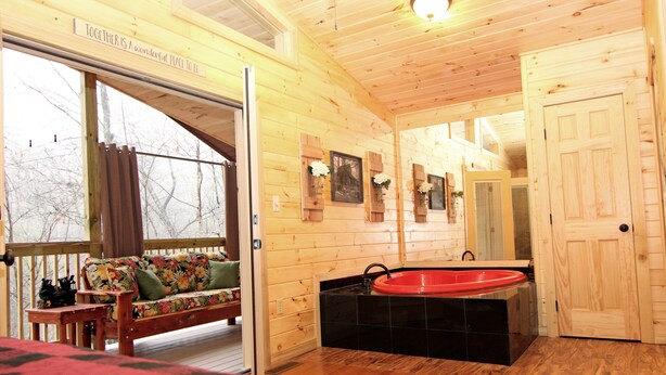 A wooden cabin interior with a wooden deck, a sofa, a red bathtub, and a door.