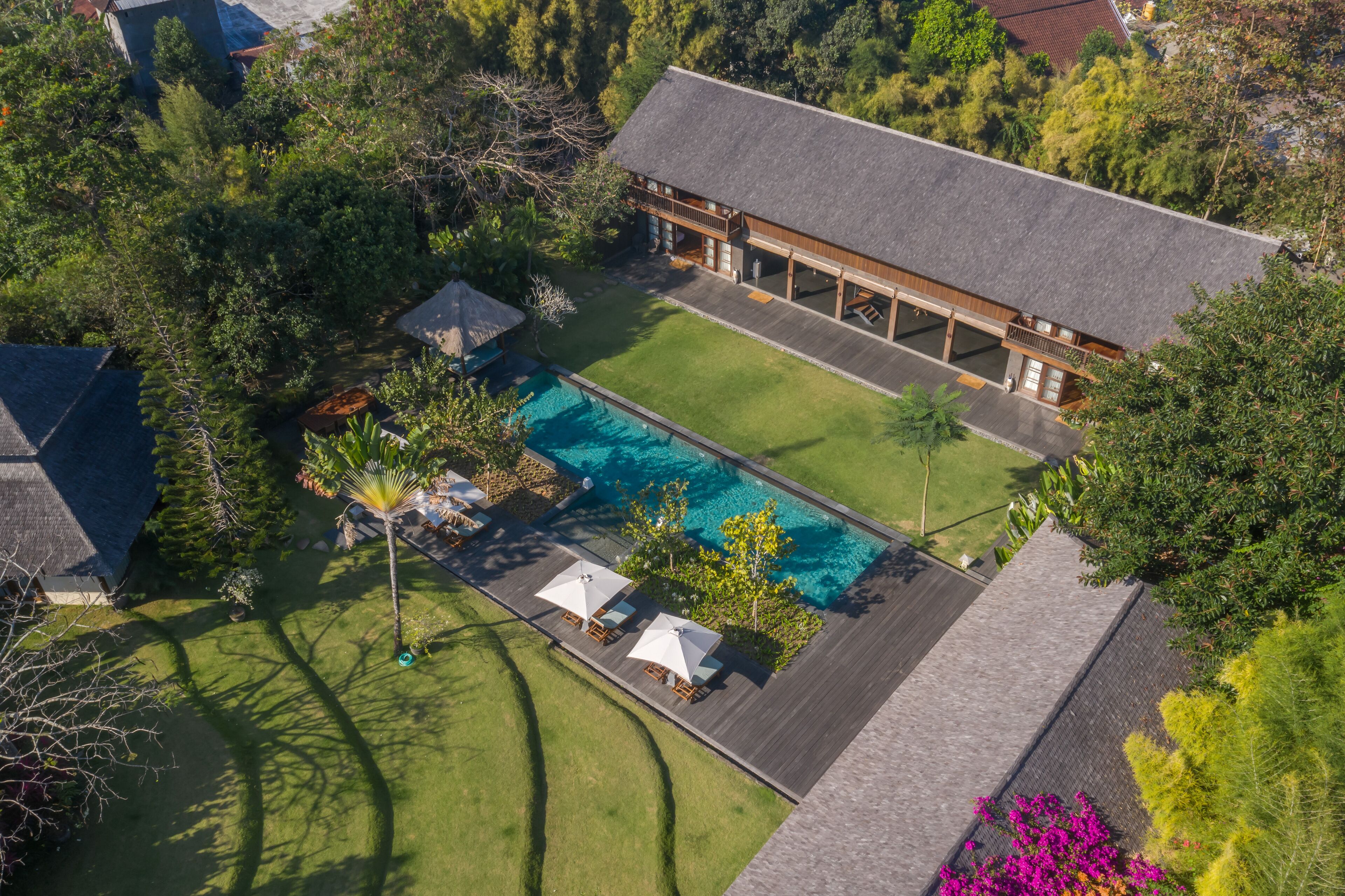 An aerial view of a house with a swimming pool, surrounded by a well-maintained lawn and trees.