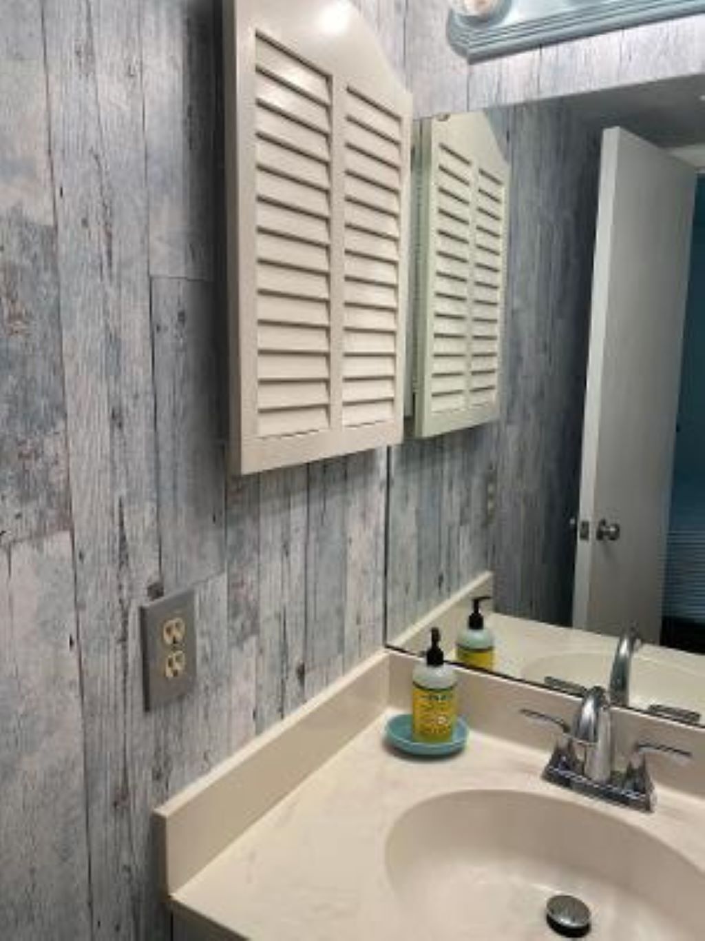 Un baño con pared de madera, un espejo, un lavabo con grifo y dos botellas de jabón.