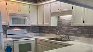 A modern kitchen with white cabinetry, a stainless steel sink, a microwave, and a stove. - INCREDIBLE OCEANFRONT VIEWS/3 BR, 3 Bath Luxury Condo/Sea Marsh I (North Myrtle Beach)