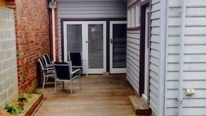 Een overdekt terras met een houten terras, twee stoelen en een bakstenen muur.