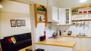 Een knus woongedeelte met een kitchenette, een zwarte bank en een eethoekje.