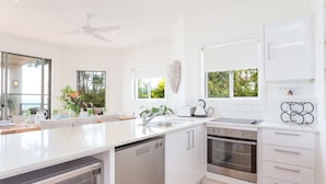 A modern kitchen with white cabinetry, a dishwasher, an oven, and a sink. - Moreton Bay Beach LodgeUnwind in  indulge in discovery (Cleveland)