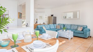 A modern living room with a teal sofa, a wooden coffee table, and a dining area with a wooden table set for a meal. - Moreton Bay Beach LodgeUnwind in  indulge in discovery (Cleveland)