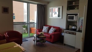 A compact living space with a red sofa, a small dining table, a kitchenette, and a sliding glass door leading to a balcony. - Nice city stay at Collins apartment (Melbourne)