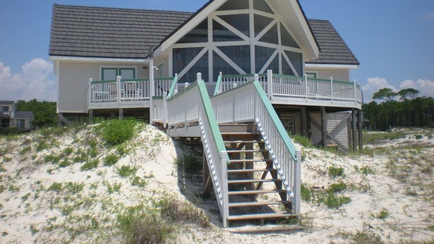 Una casa frente a la playa con un balcón destacado y una escalera que conduce a la entrada principal.