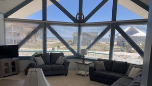Sala de estar con dos sofás, un televisor y una lámpara. Amplias ventanas ofrecen vistas a un edificio y un puente.