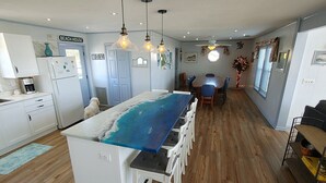 Una cocina con una isla grande, armarios blancos y un comedor con una mesa redonda y sillas.