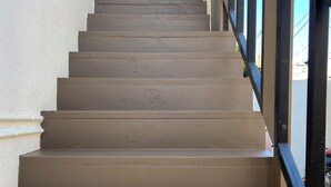 Un juego de escalones color beige con barandilla de metal que llevan a una puerta con reja de metal.