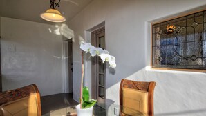 Un comedor con mesa de vidrio, dos sillas de madera, una planta blanca en maceta y un ventanal con vidrieras.