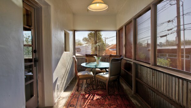 Un pasillo con un área de comedor que incluye una mesa, sillas, una lámpara colgante y ventanas grandes con vistas al exterior.