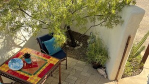 Una escalera lleva a un balcón con una mesa y sillas de cerámica, rodeado de plantas y una puerta con placa.