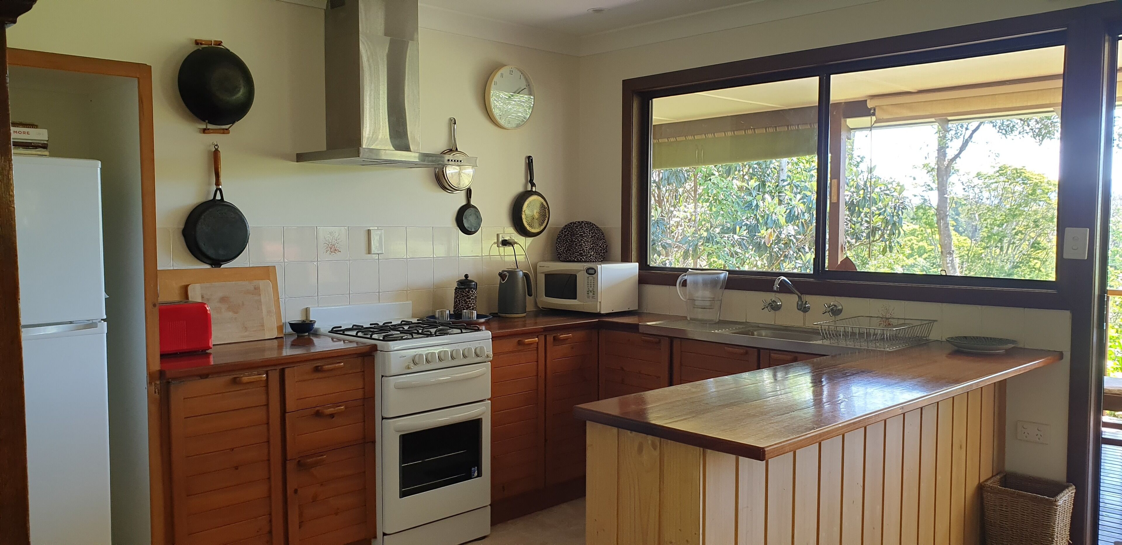 A kitchen with wooden cabinets, a stove, a microwave, and a window with a view of greenery.
