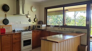 A kitchen with wooden cabinets, a stove, a microwave, and a window with a view of greenery.