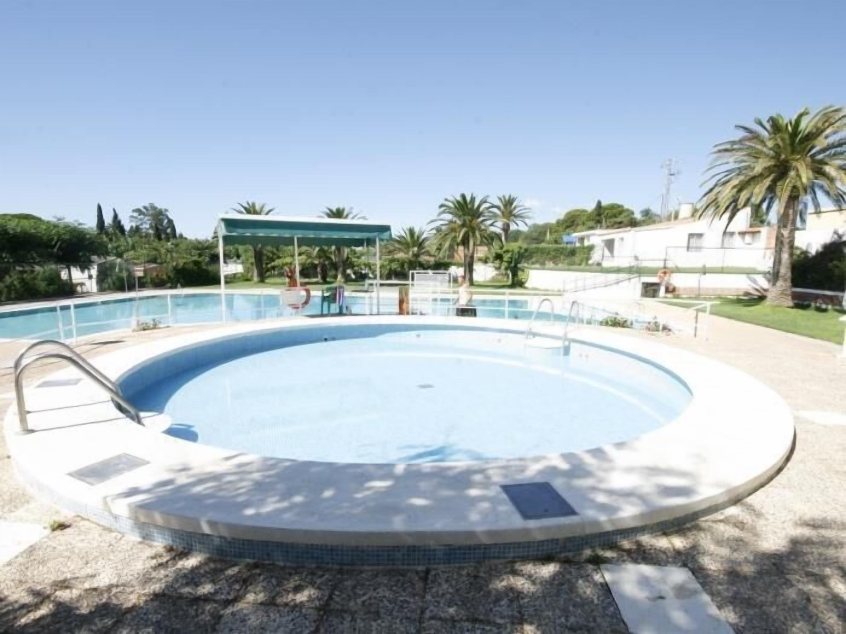 Une piscine extérieure de forme ronde, dont le bord est recouvert de carreaux, entourée d’une terrasse en béton et agrémentée d’un espace salon abrité.