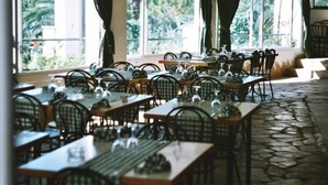 Un restaurante con varias mesas y sillas, amplios ventanales con cortinas, y un suelo con diseño de piedra.