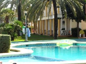 Una piscina de borde curvo, rodeada de palmeras y un edificio con columnas.