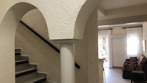 Eine Treppe mit strukturierter Wand und einer weißen Säule, die in einen Wohnbereich mit einer Couch und einer gemusterten Decke führt.