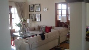 Ein Wohnzimmer mit einer Couch, einem Couchtisch und einer Lampe. An den Wänden hängen gerahmte Bilder und ein Fenster mit Vorhängen.