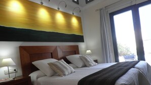 Ein Hotelzimmer mit einem großen Bett, zwei Nachttischlampen, einem Nachttisch und Blick ins Freie durch ein Fenster.