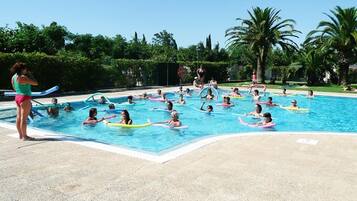 Une piscine où des personnes utilisent des bouées, entourée de palmiers et de verdure.
