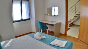 A bedroom with a bed, a desk, a chair, a window with curtains, a mirror, and a staircase. - Hot Water House 2 (Furnas)