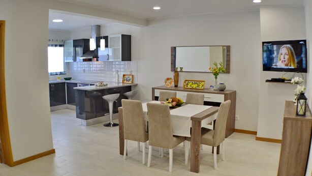A modern kitchen with white cabinets, a central island, and a dining area with a table and chairs. - Hot Water House 2 (Furnas)