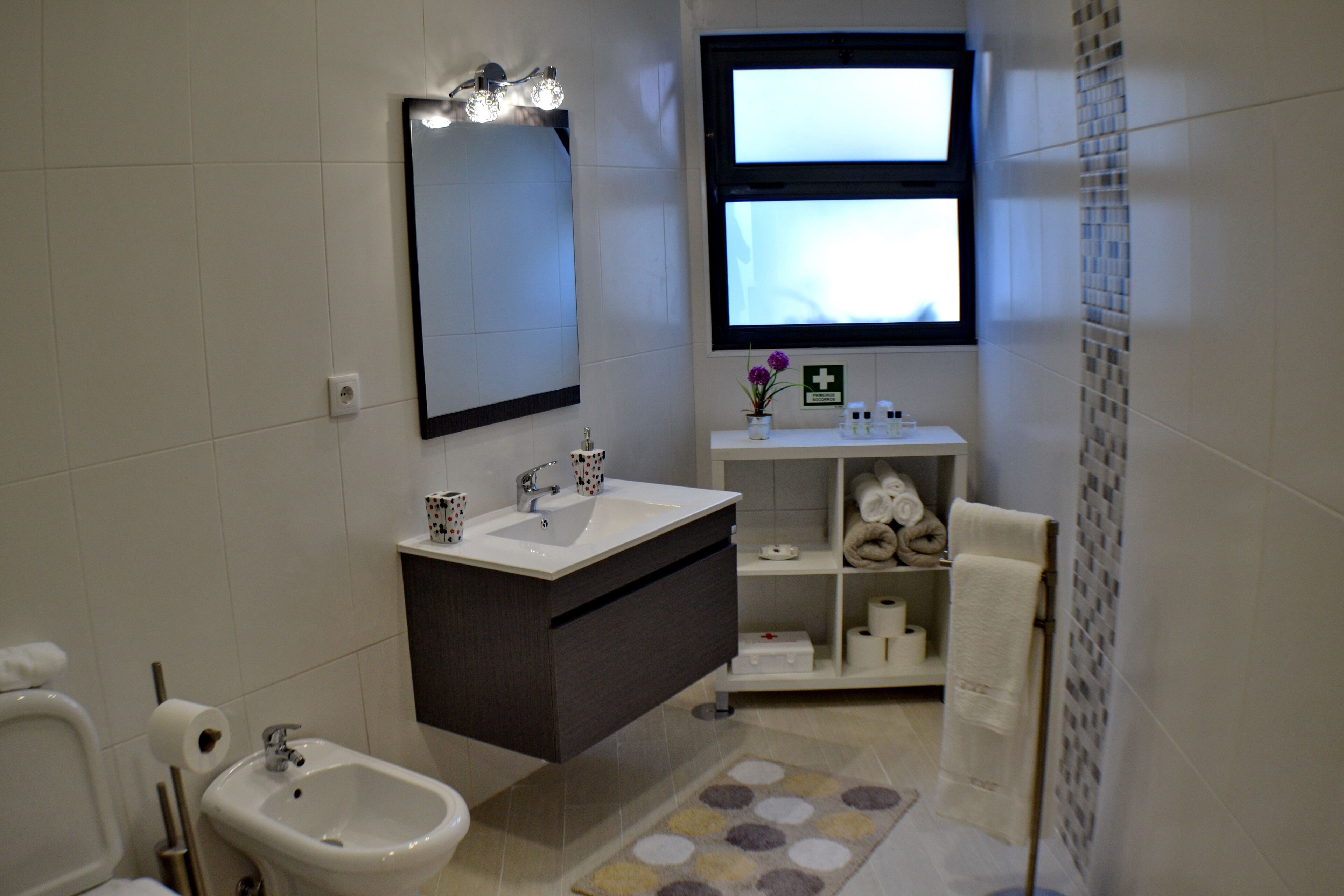 Une salle de bain moderne équipée d’un bidet, d’un lavabo, d’un miroir et d’une fenêtre.