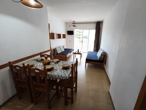 A compact living space with a dining area, a bed, and a TV. - APCOSTAS Lotus / One Bedroom (Blanes)