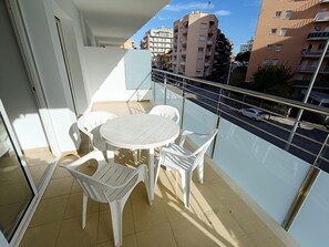 A balcony with a round table and four chairs, overlooking a street with buildings in the background. - APCOSTAS Lotus / One Bedroom (Blanes)