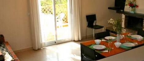 Un comedor con una mesa preparada para cuatro personas, un televisor sobre un mueble bajo y una puerta corrediza de vidrio que da a un espacio exterior.