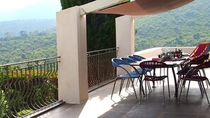 Terraço com mesa e cadeiras, com vista para uma paisagem verde exuberante.