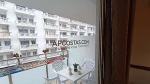 A balcony with a table and chairs, a view of a white building with balconies, and a sign reading 'APCOSTAS.COM PARTEMENTOS TURISTICOS'. - APCOSTAS Lotus / Two Bedrooms (Blanes)