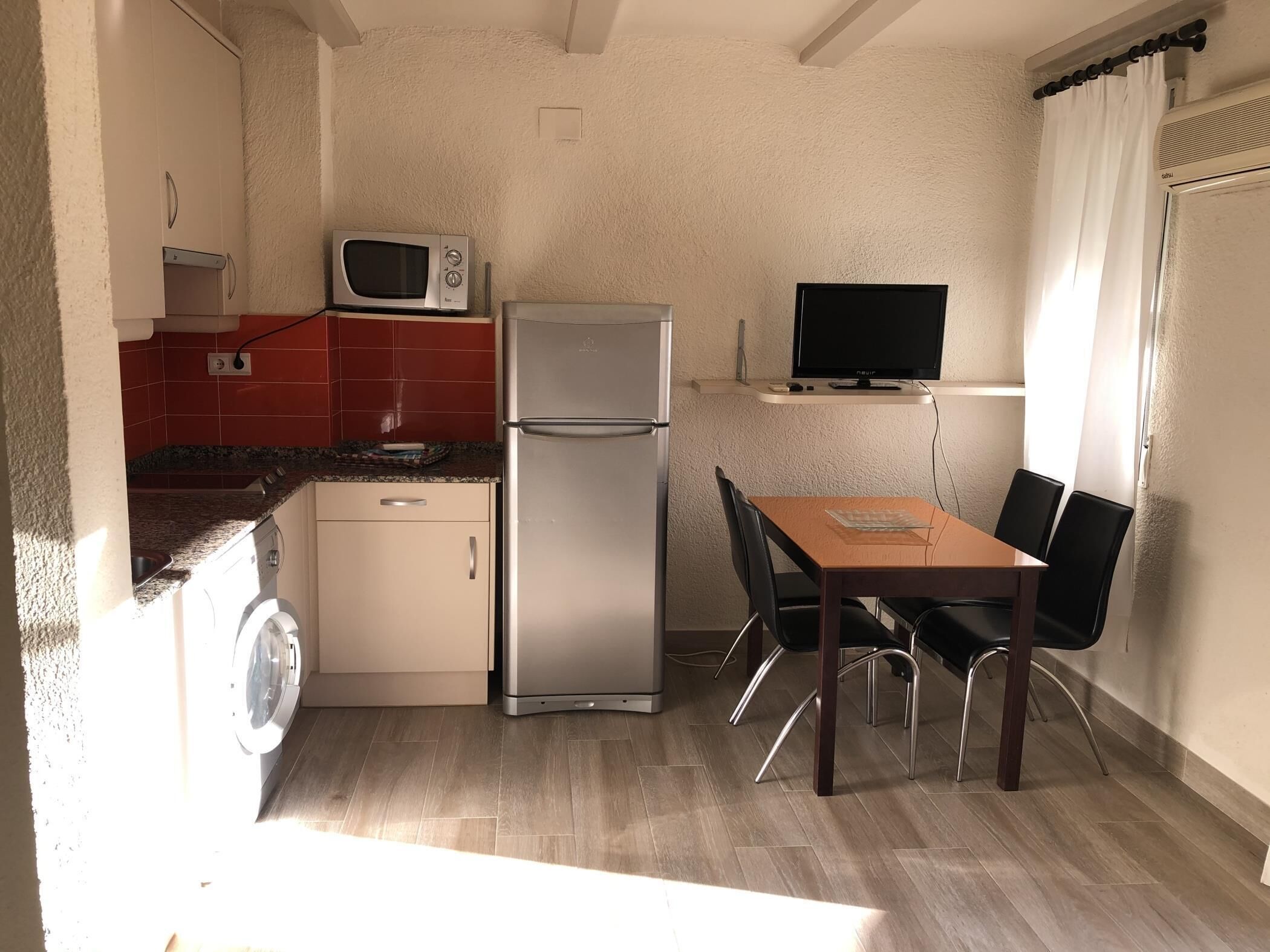A compact kitchen with a microwave, refrigerator, and a small dining table with chairs.