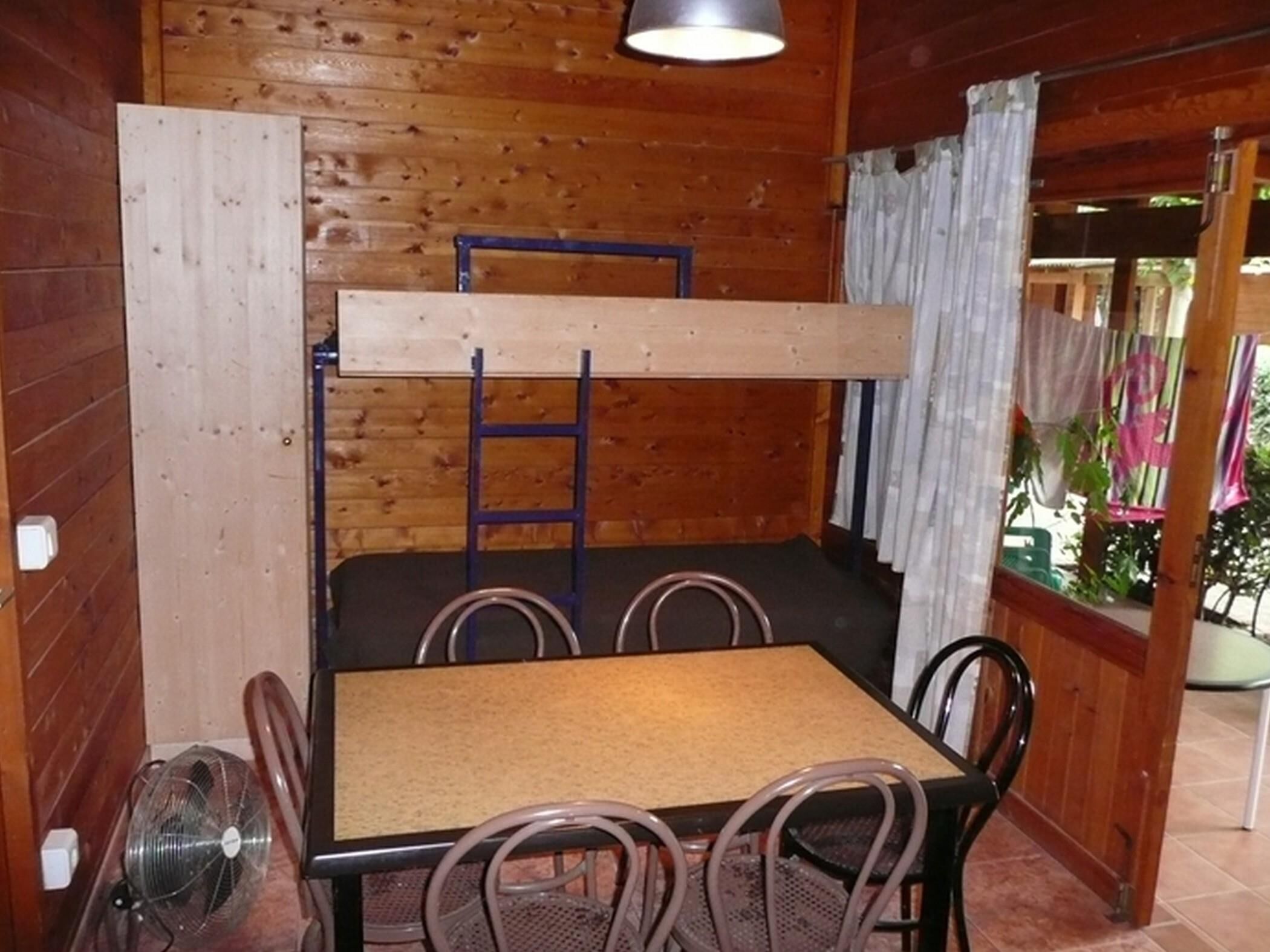 Une cabane en bois avec un lit superposé, une table, quatre chaises et un ventilateur.