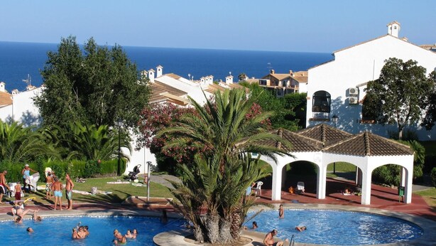 Zona de piscina con un pabellón, palmeras y vista al mar.