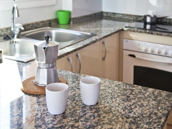 A kitchen with a granite countertop, a coffee maker, and two white cups.