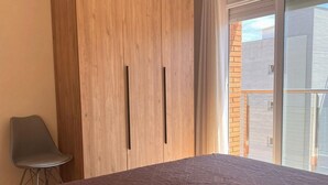A bedroom with a bed, a chair, and a wooden wardrobe. - APCOSTAS Villa De Madrid / Two Bedrooms (Blanes)