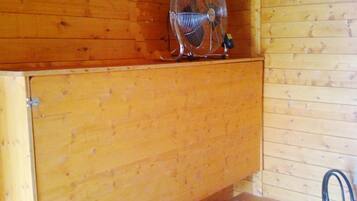 Une pièce en bois avec un ventilateur posé sur une étagère, un banc et une chaise en métal.
