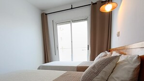 A hotel room with two beds, a window with curtains, and a wall-mounted light fixture. - APCOSTAS Lotus / Two Bedrooms (Blanes)