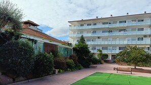 A courtyard with a green lawn, a bench, and a building with multiple balconies. - APCOSTAS Lotus / Two Bedrooms (Blanes)