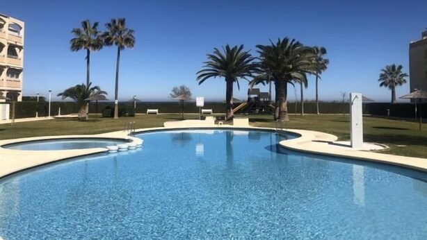 Une piscine à l’eau d’un bleu cristallin, entourée de palmiers et avec un bâtiment visible au loin.