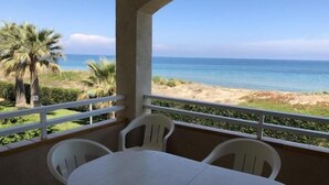 Un balcon avec une table et des chaises, donnant sur une plage bordée de palmiers et sur l’océan.