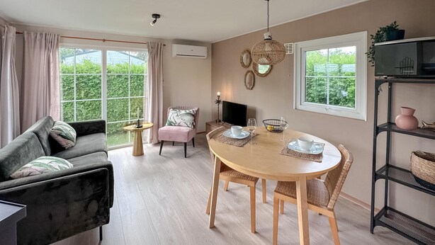 Een gezellige woonkamer met een bank, een roze fauteuil, een houten eettafel met stoelen, een televisie en een boekenkast.
