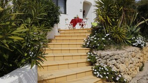 A set of stone steps leading to a white building with a red table and chairs outside. - Apartment Al Gharb (Carvoeiro)