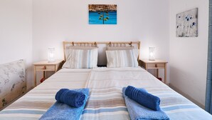 A double bed with striped bedding, two bedside tables with lamps, and artwork on the walls. - Apartment Al Gharb (Carvoeiro)