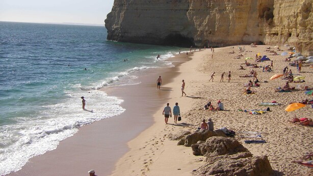 A beach with people sunbathing and swimming, cliffs in the background, and a clear sky. - Apartment Al Gharb (Carvoeiro)