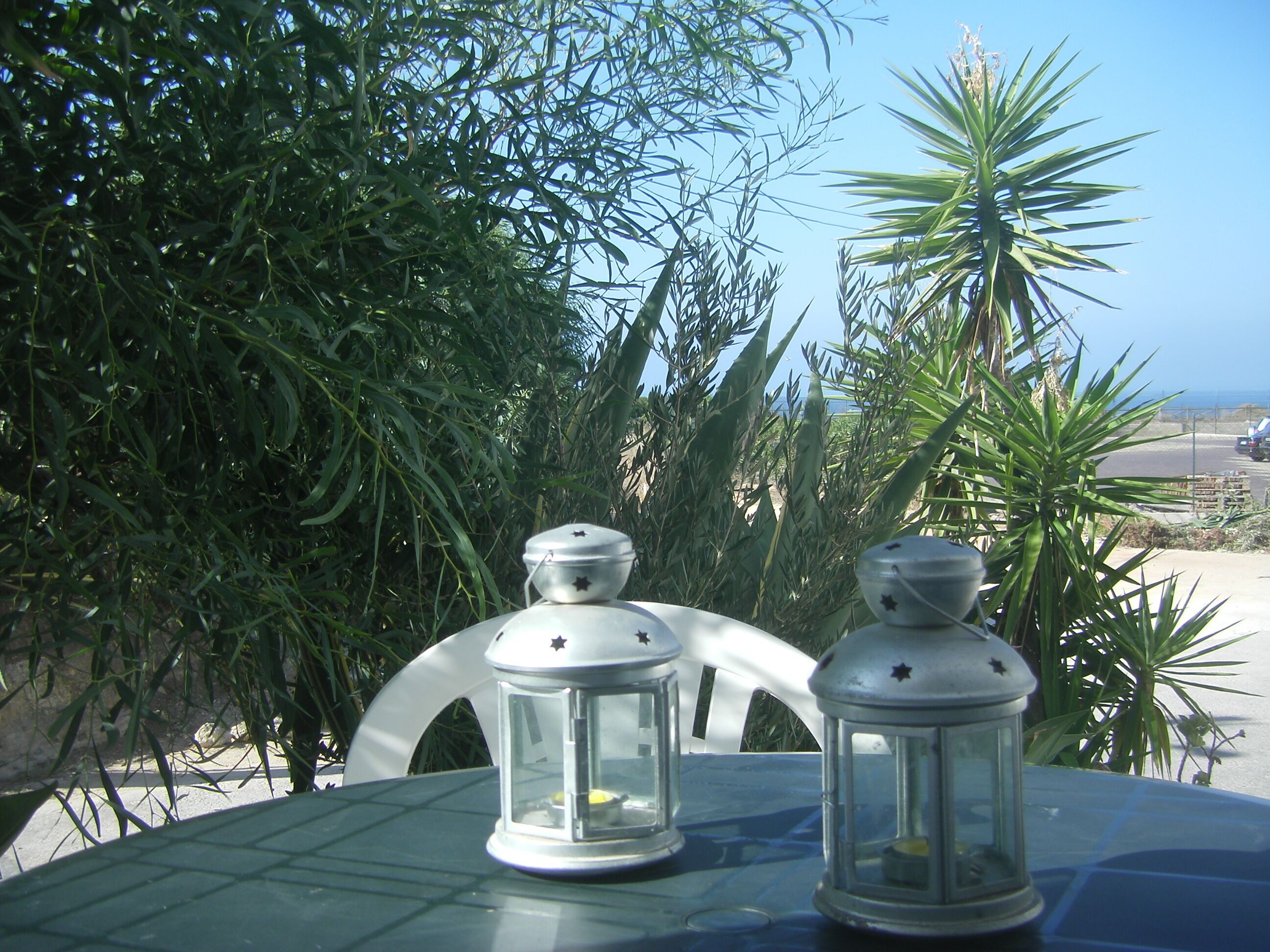 Two white lanterns on a table with a clear view of a palm tree and a road in the background.