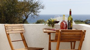 A wooden table with two chairs, a bottle of wine, and a glass of red wine on a balcony with a view of the sea. - Apartment Al Gharb (Carvoeiro)